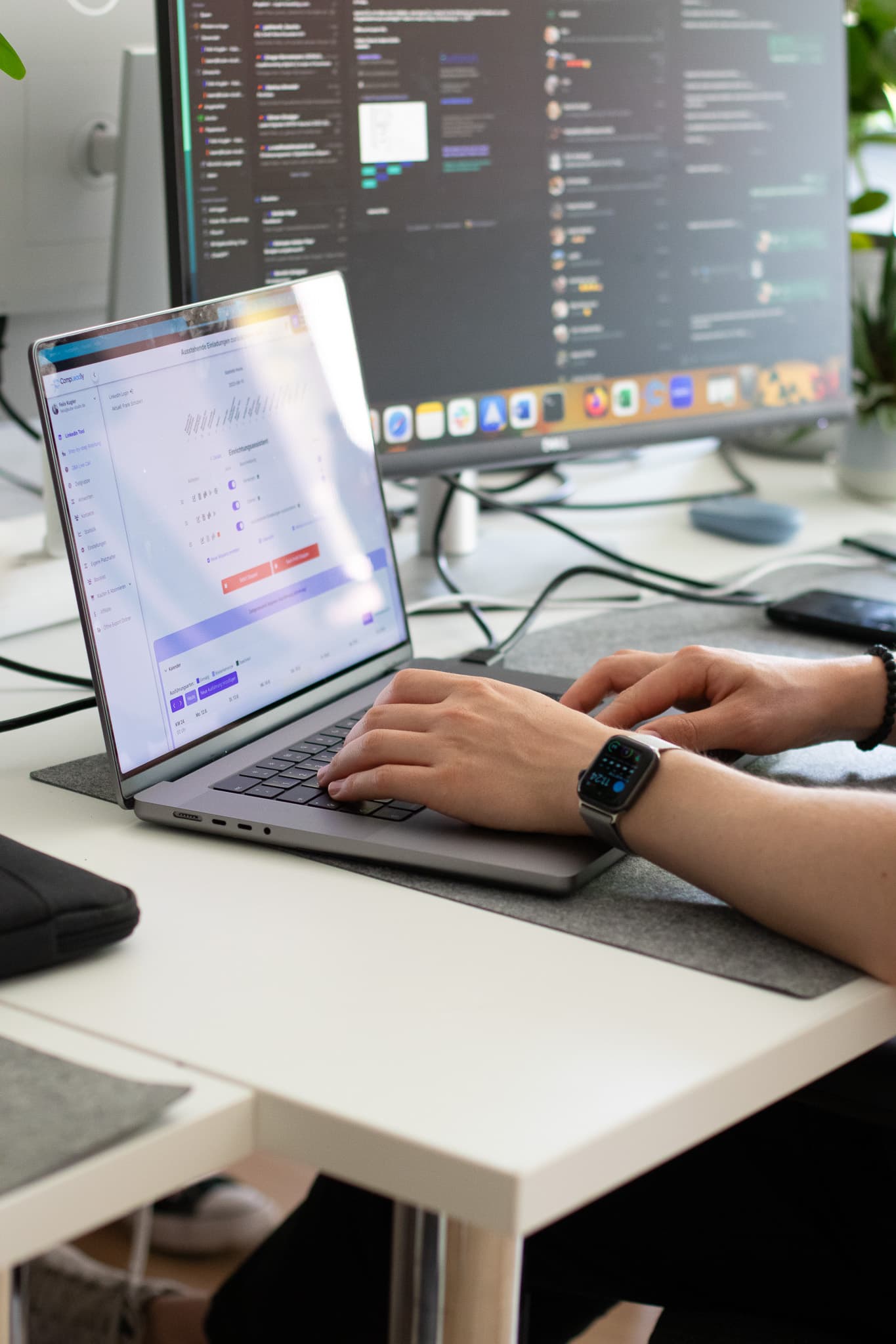 Hand tippt auf Laptop mit Minitor im Hintergrund